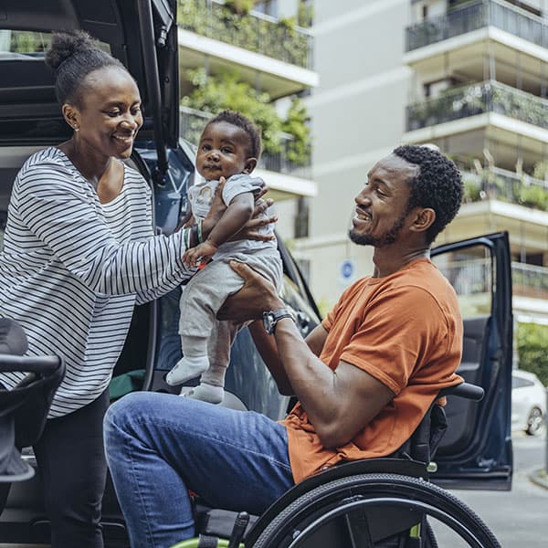 A man in a wheelchair hands a baby to a woman..