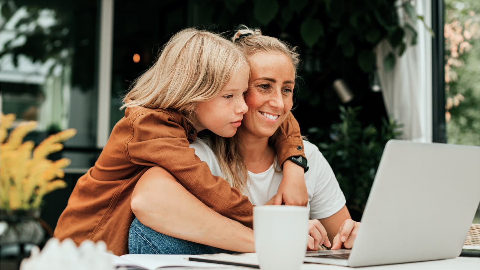 Smiling woman using laptop with son embracing her