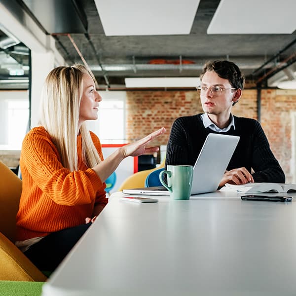 Woman speaking to her co-worker at her desk.