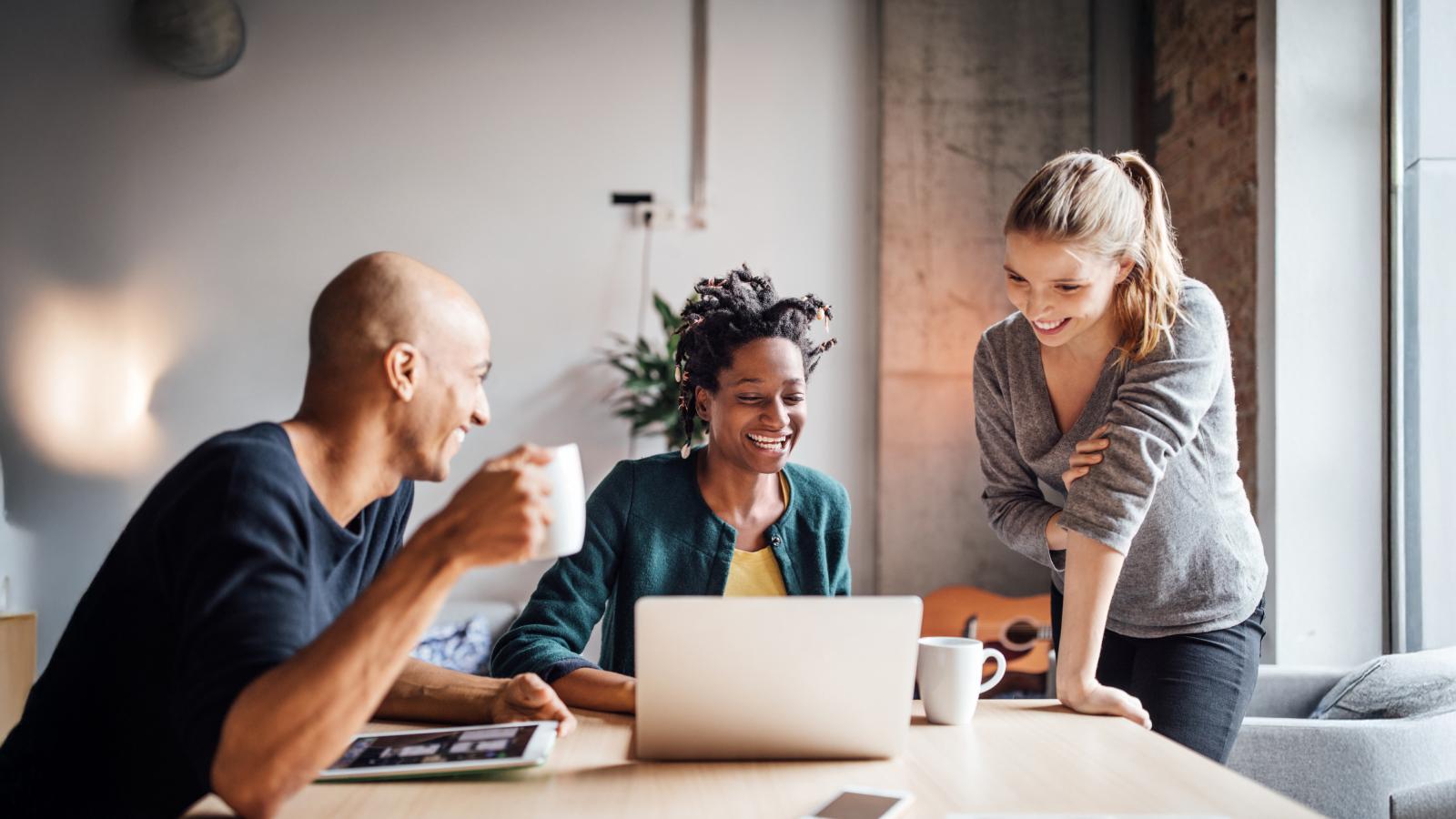 Three employees smiling while looking at a computer together.