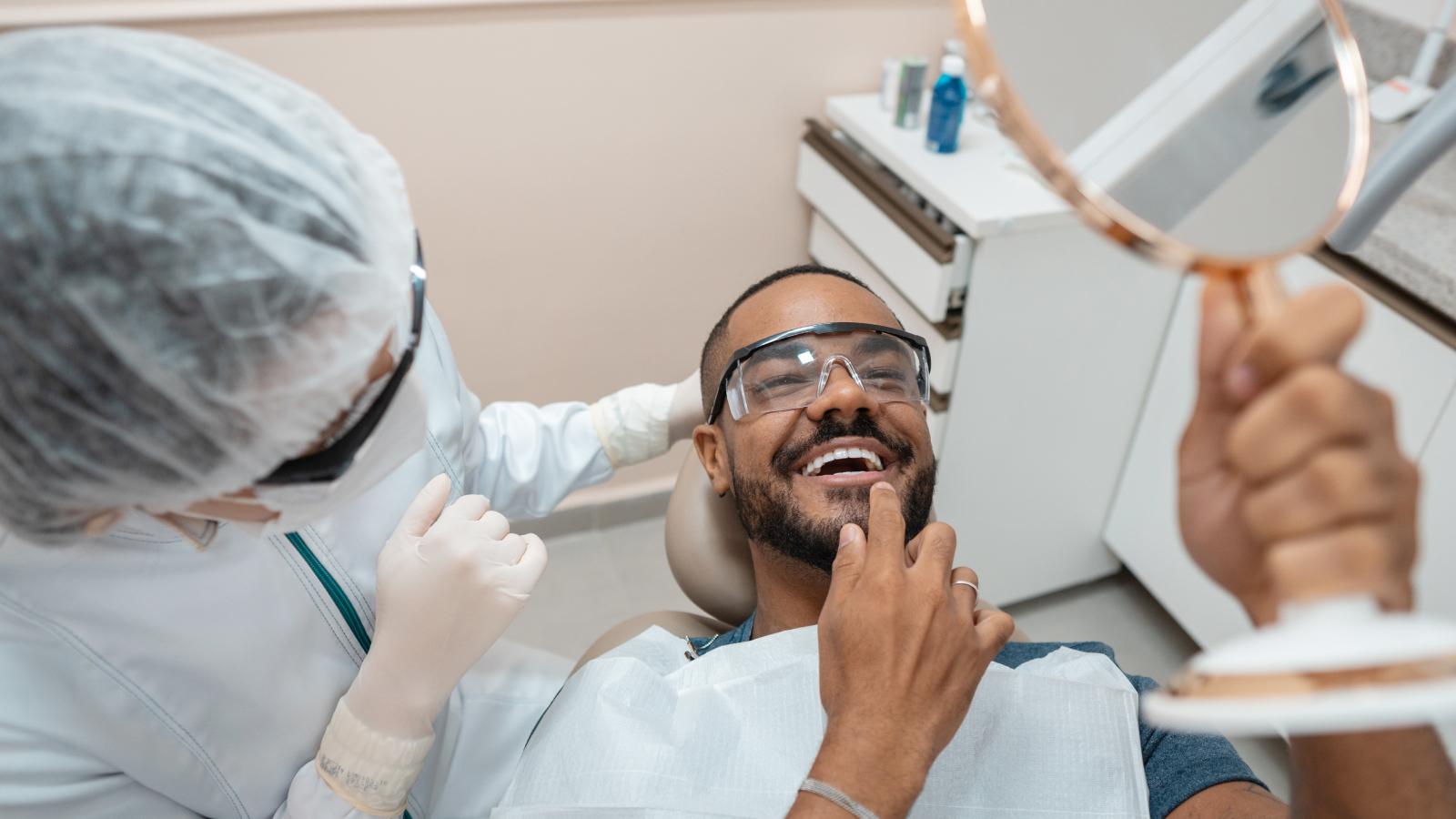 Patient smiling in a mirror with dentist looking on.