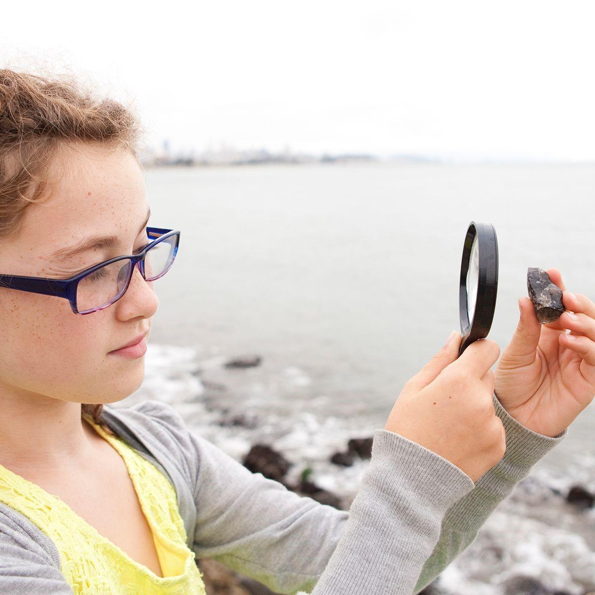 Young girl examines rock through magnifying glass.
